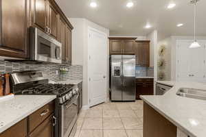 Kitchen with appliances with stainless steel finishes, light stone countertops, pendant lighting, dark brown cabinetry, and recessed lighting