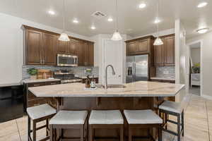 Kitchen featuring dark brown cabinets, appliances with stainless steel finishes, a kitchen breakfast bar, a center island with sink, and recessed lighting