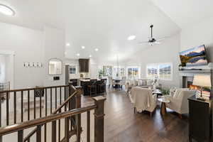 Living area with dark wood-style floors, a warm lit fireplace, high vaulted ceiling, and a ceiling fan