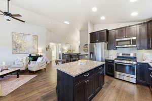 Kitchen with open floor plan, appliances with stainless steel finishes, dark brown cabinetry, a kitchen island, and light stone countertops