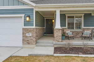 Doorway to property featuring a porch, roof with shingles, a garage, and brick siding