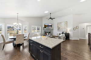 Kitchen featuring a fireplace, light stone countertops, open floor plan, dark wood-type flooring, and high vaulted ceiling