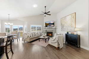 Living area with hardwood / wood-style floors, a lit fireplace, high vaulted ceiling, ceiling fan, and a chandelier