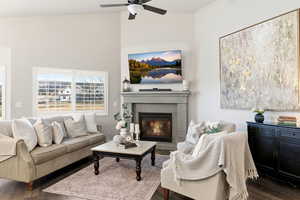 Living room featuring a glass covered fireplace, dark wood-style flooring, high vaulted ceiling, and a ceiling fan