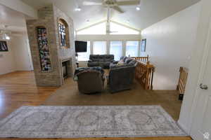 Living room featuring a ceiling fan, a brick fireplace, light wood-type flooring, and beamed ceiling