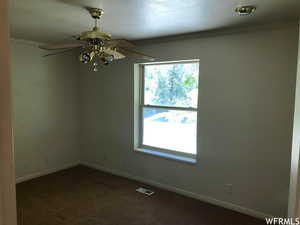 Spare room with ornamental molding, dark colored carpet, and a ceiling fan
