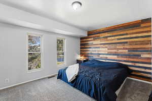 Carpeted bedroom featuring wooden walls and an accent wall