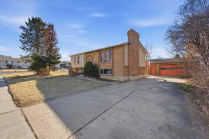 View of front of home with a chimney, driveway, brick siding, and an outdoor structure