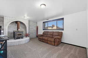 Living area with carpet floors, a wood stove, brick wall, and a textured ceiling