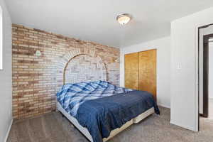 Bedroom with brick wall, carpet floors, an accent wall, and a closet