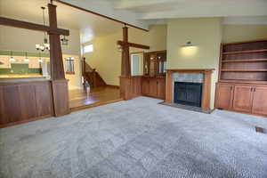 Unfurnished living room with carpet flooring, a tile fireplace, beam ceiling, a chandelier, and stairs