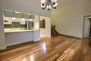 Kitchen with light countertops, white cabinetry, hardwood / wood-style floors, freestanding refrigerator, and a chandelier