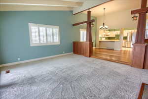 Unfurnished living room with carpet flooring, a chandelier, and decorative columns