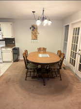 Dining room featuring a textured ceiling, french doors, suspended lighting, light colored carpet, and light tile patterned flooring