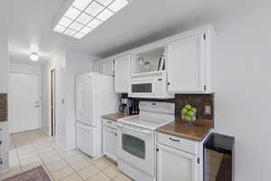 Kitchen with white appliances, dark countertops, tasteful backsplash, white cabinetry. Appliances included.