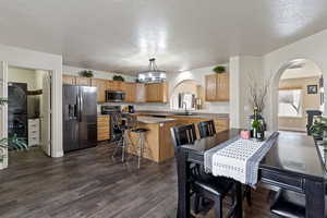 Dining space with arched walkways, stacked washer / drying machine, a textured ceiling, dark wood-type flooring, and a chandelier