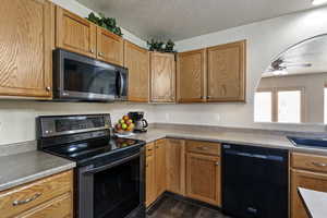 Kitchen with appliances with stainless steel finishes, a textured ceiling, brown cabinets, ceiling fan, and light countertops