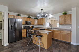 Kitchen featuring appliances with stainless steel finishes, a center island, decorative light fixtures, a chandelier, and a breakfast bar