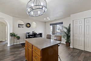 Kitchen with brown cabinetry, a center island, arched walkways, a breakfast bar, and dark wood-style floors