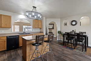 Kitchen with arched walkways, dishwasher, a kitchen island, a breakfast bar, and hanging light fixtures