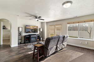 Living room featuring arched walkways, a glass covered fireplace, dark wood finished floors, ceiling fan, and a textured ceiling