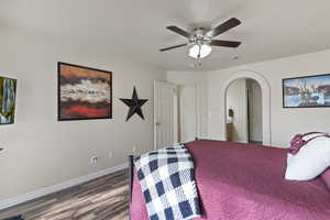 Bedroom with wood finished floors, a ceiling fan, ensuite bath, and arched walkways