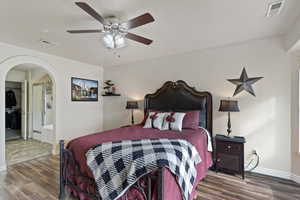 Bedroom with arched walkways, ceiling fan, wood finished floors, and ensuite bath