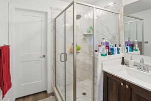 Bathroom with vanity, a marble finish shower, and wood finished floors