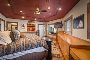 Bedroom featuring dark wood-type flooring, a raised ceiling, ceiling fan, and ornamental molding