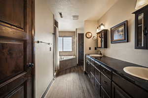 Full bath with a textured wall, a textured ceiling, dark wood-type flooring, a bath, and double vanity