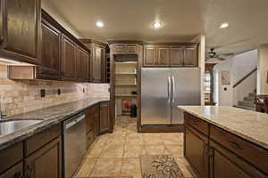 Kitchen with dark brown cabinetry, appliances with stainless steel finishes, recessed lighting, dark stone countertops, and decorative backsplash