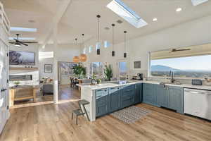 Kitchen featuring a ceiling fan, a peninsula, stainless steel dishwasher, light stone countertops, and a skylight