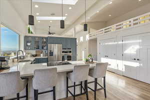 Kitchen with a peninsula, decorative light fixtures, stainless steel appliances, glass insert cabinets, and light wood-style floors