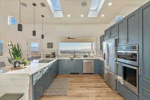 Kitchen with decorative light fixtures, stainless steel appliances, a peninsula, light wood-type flooring, and light stone countertops
