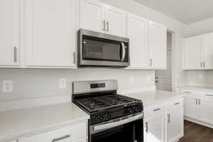 **DISCLAIMER** Interior color package may vary.Kitchen with stainless steel appliances, white cabinetry, light stone counters, and dark wood-style floors