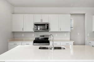 **DISCLAIMER** Interior color package may vary.Kitchen featuring stainless steel appliances, white cabinetry, light stone countertops, and an island with sink