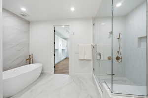 Full bath featuring a stall shower, recessed lighting, a freestanding tub, marble look tiles, and tile walls