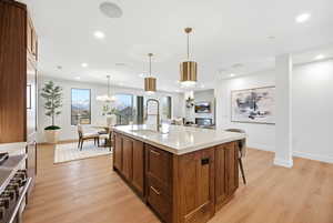 Kitchen with light wood-style floors, brown cabinetry, high end stainless steel range oven, a kitchen island with sink, and recessed lighting