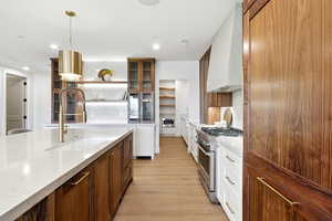 Kitchen with brown cabinetry, light stone counters, high end range, decorative light fixtures, and custom range hood