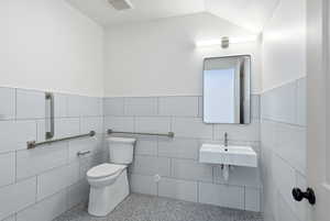 Bathroom with speckled floor, tile walls, wainscoting, and vaulted ceiling