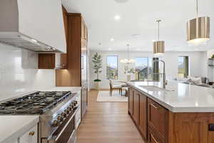 Kitchen with brown cabinets, exhaust hood, open floor plan, stainless steel range, and light stone counters