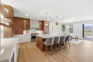 Kitchen with brown cabinets, decorative light fixtures, light wood-style flooring, high end stove, and tasteful backsplash