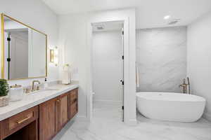 Full bathroom featuring vanity, a freestanding tub, recessed lighting, and light marble finish flooring