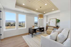Home office featuring a raised ceiling, light wood finished floors, wooden ceiling, a mountain view, and recessed lighting