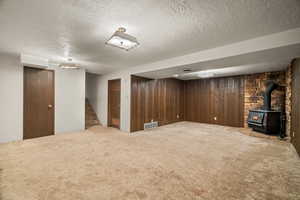 Finished below grade area with a wood stove, a textured ceiling, carpet flooring, stairway, and wood walls