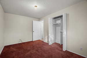 Unfurnished bedroom with a textured ceiling, carpet, and a closet