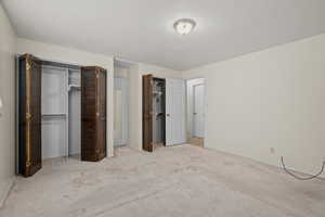 Unfurnished bedroom featuring two closets, a textured ceiling, and light colored carpet