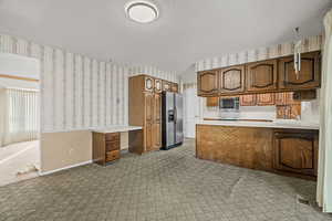 Kitchen with wallpapered walls, a peninsula, brown cabinets, light countertops, and a textured ceiling