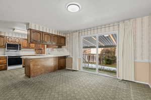 Kitchen featuring wallpapered walls, light countertops, a textured ceiling, range with electric cooktop, and a peninsula