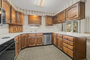 Kitchen featuring wallpapered walls, a peninsula, light countertops, stainless steel dishwasher, and a textured ceiling